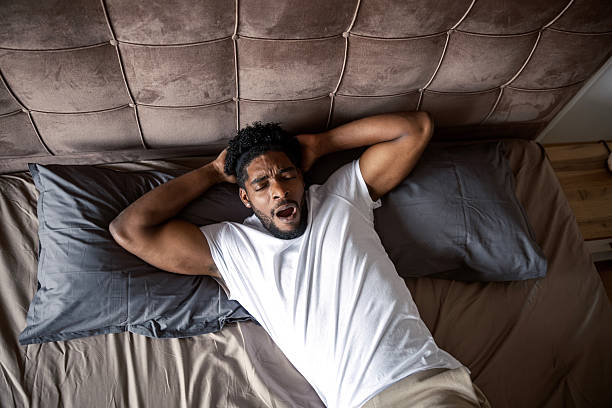 istock Young man yawning in bed feeling tired in the morning 2249573748