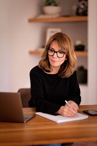 istock Blond haired middle-aged woman sitting at home and using her laptop 2249577069