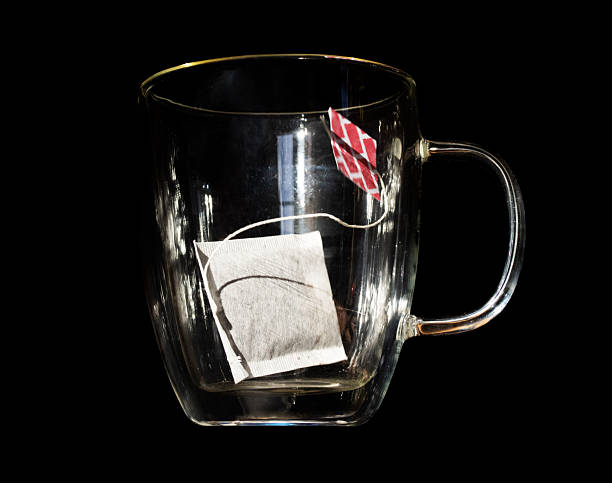 A bag of tea falls into an empty glass mug on a black background
