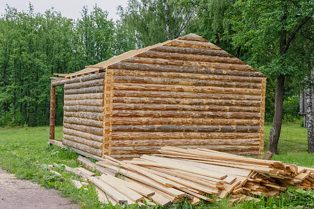A wooden log house with boards for building a roof lying in the foreground