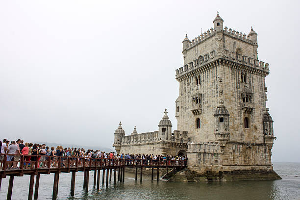 Lisbon, Portugal. Full view of Belem Tower with its wooden entry walkway packed with visitors on an overcast day, highlighting heavy tourist traffic around this Manueline riverside fortification