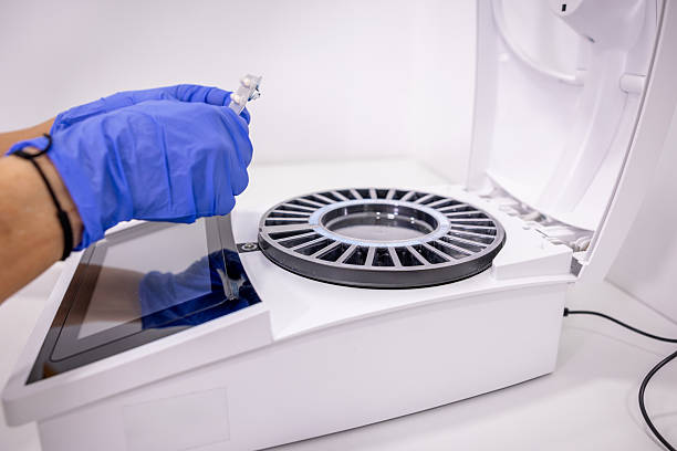 Hand in blue protective gloves inserting a small vial into a cutting-edge automated analyzer, performing sample analysis for medical diagnostics, scientific research, and pharmaceutical developments