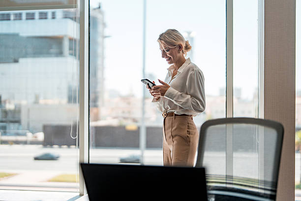 istock Professional Businesswoman Using Smartphone By Large Office Windows In Natural Light 2249586055