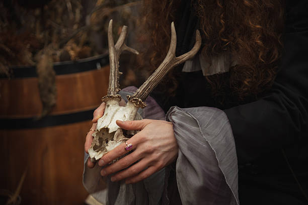 A person with curly hair gently holds an animal skull featuring antlers. The setting is dimly lit, with wooden barrels in the background, creating a mysterious atmosphere.