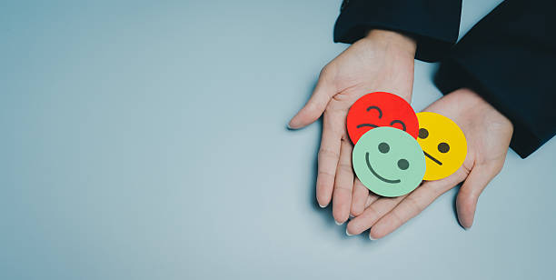 istock Colorful paper smiley face held in hands, representing different emotions and feelings with red, green, and yellow colors on blue background, conveying mood and expression 2249586518
