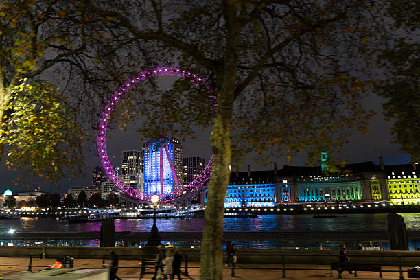 London, UK - December 23 2025: The illuminated London Eye and Big Ben glow against a dark cloudy night sky with lights reflecting on the River Thames as seen from the Golden Jubilee Bridges