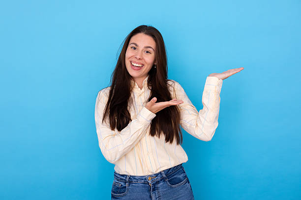 istock Happy young woman smiling, presenting important information with open palms on a blue background 2249593585