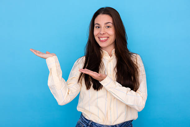 istock Smiling woman presenting marketing content or product with open hands on blue background, copy space 2249593587