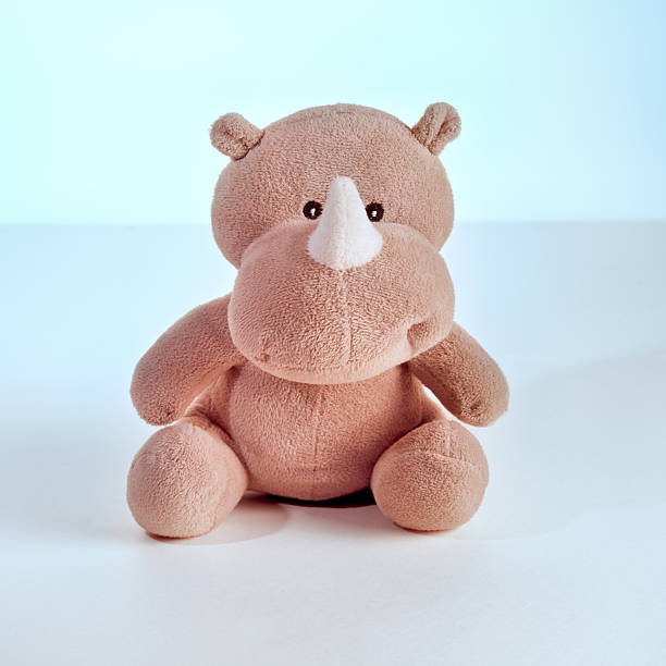 A cute, soft plush rhino toy sits on a clean white surface against a gentle blue background. This adorable animal figure evokes childhood innocence and playfulness in a minimalist studio setting.