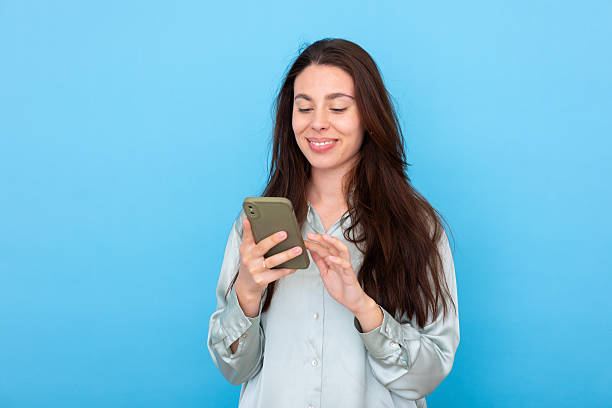 istock Young adult woman using smartphone, happily browsing content on blue background, enjoying digital connection 2249598152
