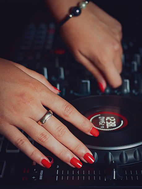 Image of a girl's hands with red nails and bracelets, using a black DJ mixing console