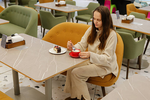 A girl sits comfortably in a trendy cafe, savoring her dessert and coffee. The bright surroundings enhance her delightful experience during the afternoon