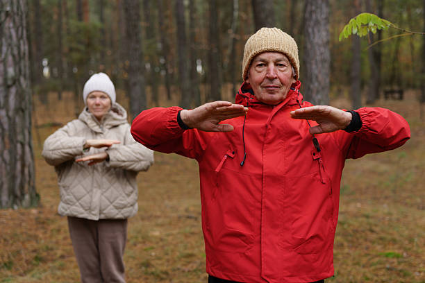 istock Two seniors are practicing Tai Chi in a peaceful forest setting. They are surrounded by tall trees and fallen leaves, creating a serene atmosphere 2249607139