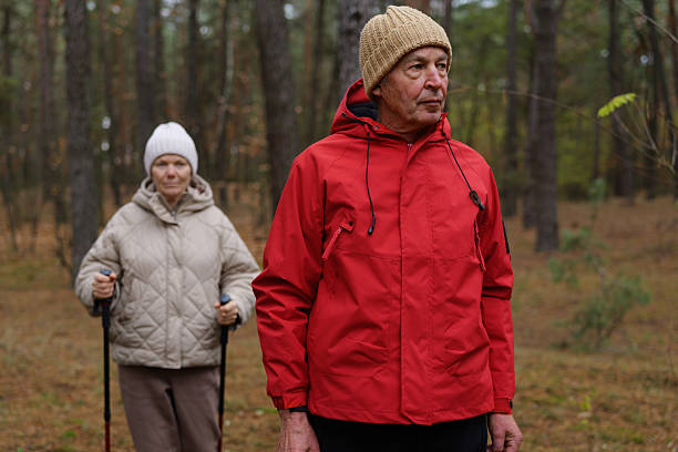istock Two elderly people are walking in a serene forest, surrounded by tall trees and autumn foliage, dressed warmly for the cool weather 2249607143