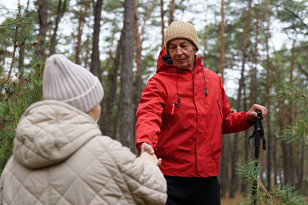 istock An elderly man wearing a red jacket greets a woman in a cozy coat while walking in the forest. The trees provide a serene backdrop in winter 2249607147