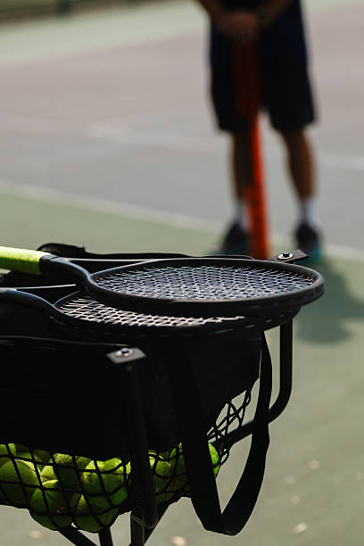 istock Tennis equipment rests on a netted cart while a player prepares to serve during a sunny afternoon on the court 2249617613