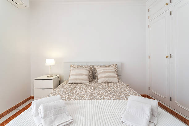 istock A well-lit bedroom features a double bed with striped pillows and freshly arranged towels. A bedside table holds a lamp, against crisp white walls and a neat closet 2249621816