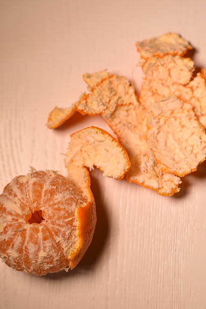 Vertical top view showing an almost peeled mandarin on a light surface, with a whole mandarin bottom-left and peel curling toward the top-right, minimal composition.