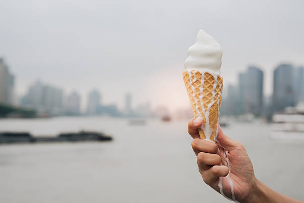 Melting ice cream cone held by hand with blurred cityscape background, soft light and warm feeling on cloudy day by river