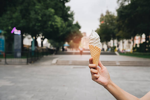 istock Soft serve ice cream cone held by hand in outdoor park setting with trees and walkway, evoking warm and joyful summer day experience 2249632863