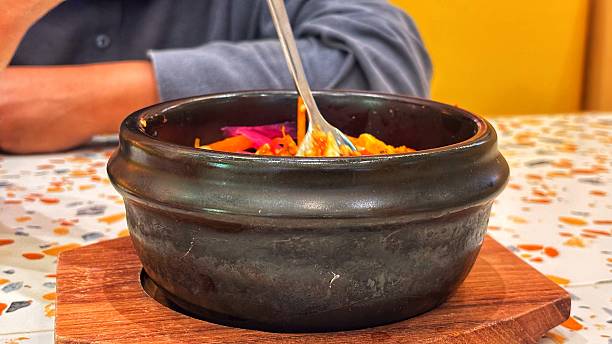 A black stone bowl holds a vibrantly colored dish, likely Bibimbap, served on a wooden trivet. A warm and inviting Korean meal
