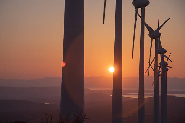 A striking silhouette of wind turbines under a warm, orange sunset sky. The image captures the renewable energy landscape at dusk, signifying clean energy, environmental innovation, and sustainable development in a serene, open-air setting.