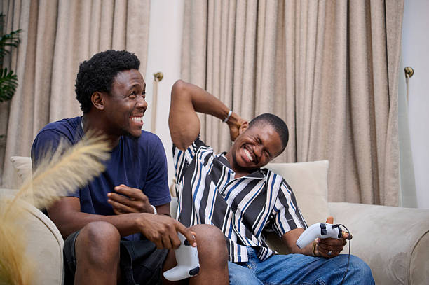 istock Two men laughing while playing video games on a couch at home 2249637411