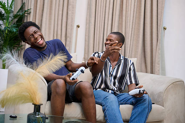 istock Two young men laughing together while playing video games on a couch at home 2249637412