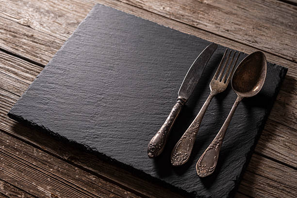 istock Retro metal cutlery on granite surface over aged wooden background. 2249637457