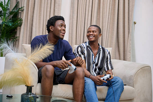istock Two young men smiling while playing video games together on a couch indoors 2249637712