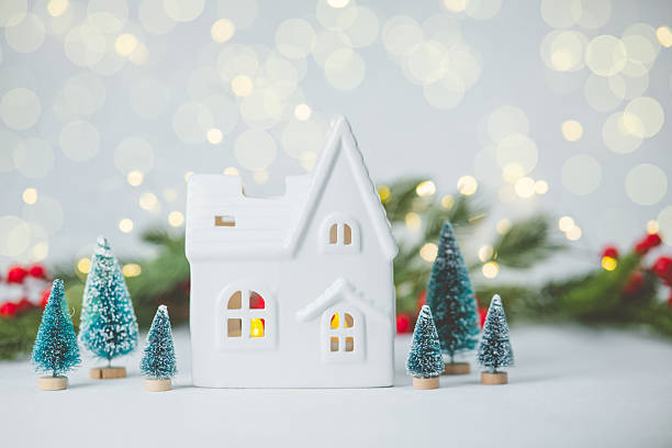 istock White miniature house surrounded by pine trees and festive lights 2249640427
