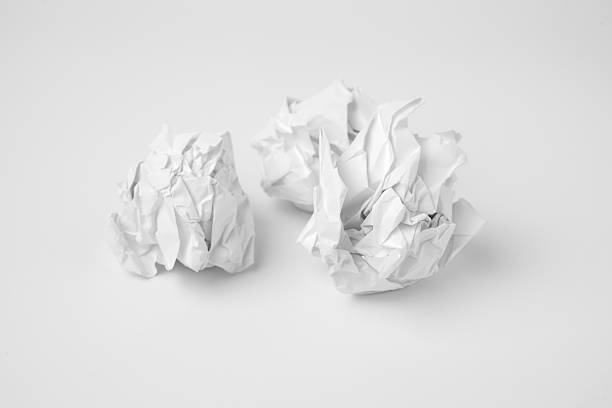 Minimal top-view image featuring two white crumpled paper balls placed on a clean white surface. The subtle shadows emphasize the irregular folds and texture. The monochromatic composition conveys themes of discarded ideas, creativity, and simplicity.