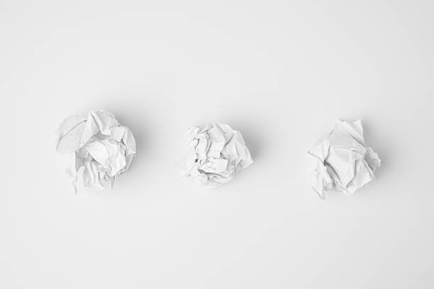 Top-view minimalist composition featuring three white crumpled paper balls aligned horizontally on a clean white surface. The subtle shadows emphasize the irregular shapes and textures. The monochromatic scene evokes creativity, discarded ideas, and simplicity.