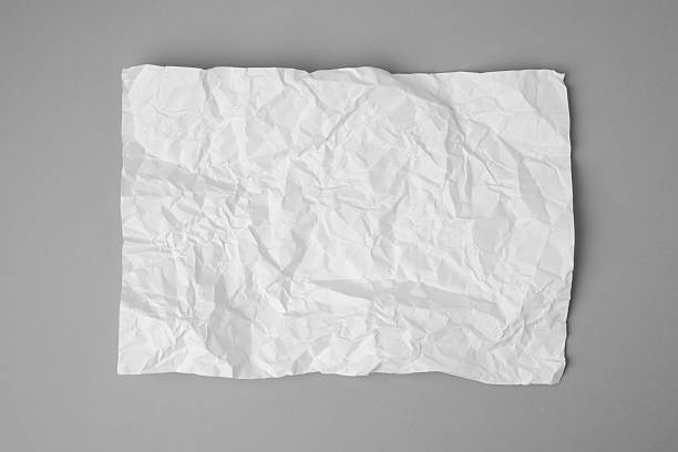Top-view image of a white, crumpled sheet of paper lying on a smooth gray background. The irregular folds and creases create a rich texture that contrasts with the clean, neutral surface. The minimalist composition evokes themes of discarded ideas, creativity, and imperfection.