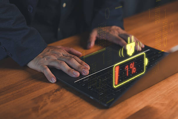 Close-up of hands on a laptop computer with a glowing low-battery warning icon at 1%. Concept of technology failure, digital burnout, device charging issues, energy crisis and urgent solutions.