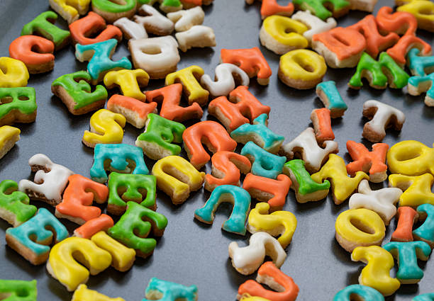 Bright, letter-shaped cookies with multicolored icing scattered on a dark surface. A fun, playful bakery scene perfect for kids parties, baking, and colorful snack ideas.