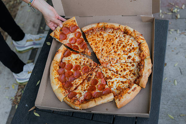 Hand picking pepperoni pizza slice from takeout box