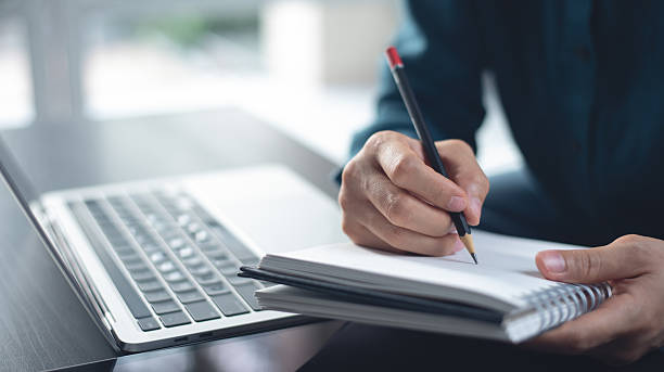 istock Hand with pencil writing on notebook. Female student studying online class via laptop computer and writing note on paper notebook. Business woman working on laptop computer, searching the ideas and taking note, business plan, e-learning, close up 2249652585