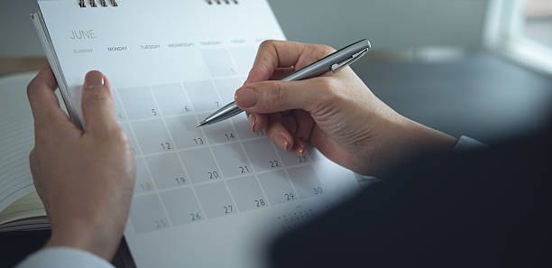 istock 2026 Calendar event planning timetable agenda plan on organize schedule. Event planner agenda organizing by organizer schedule. Business woman hand writing on calendar planner on office table, closeup 2249653856