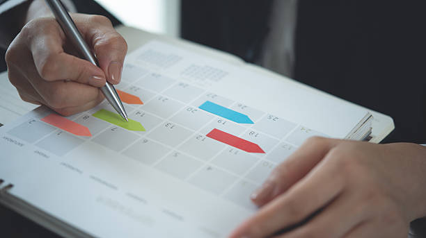 istock Closeup, woman hand writing on calendar event planner to set timetable organize schedule, event planning for business meeting or vacation plan. Organization and business planning concept. 2249654048