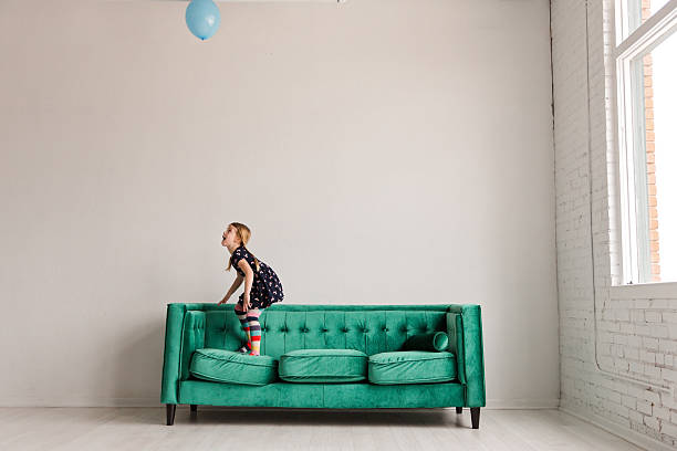 Girl balancing on green couch while playing with blue balloon indoors in Dallas, Texas, United States