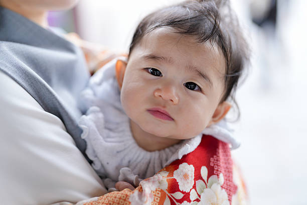 A baby is being held by a woman. The baby has a red and white outfit on. The baby has a serious expression on its face