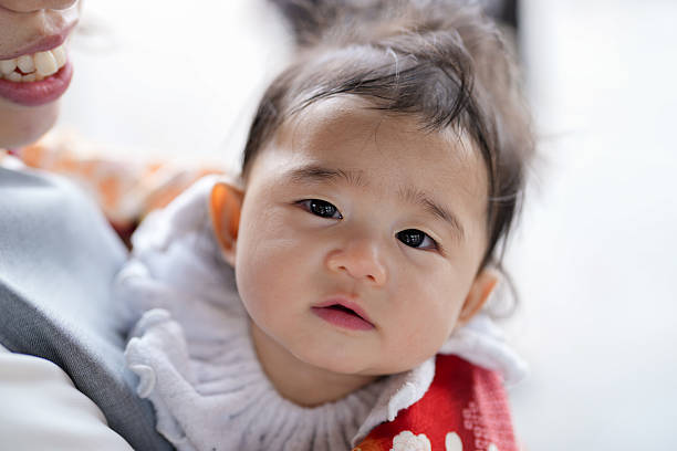 A baby is wearing a white shirt and a red blanket. The baby is looking at the camera with a serious expression