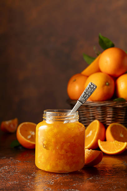 Orange jam and fresh fruits on a brown vintage table.