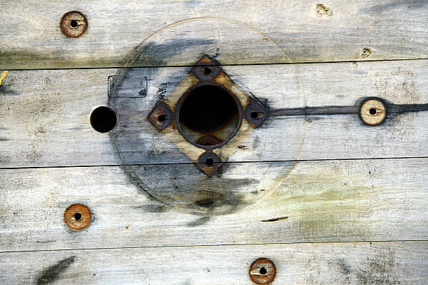 Closeup of weathered wooden breakwater with rusty bolts and stones wedged between planks