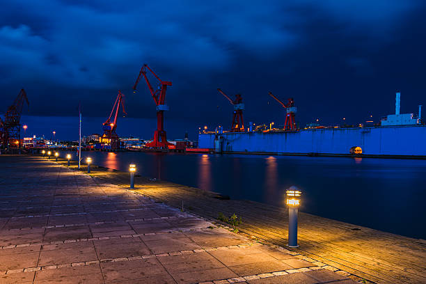 Illuminated shipyard at dusk with crane and dock.
