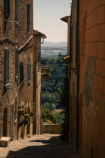 sunlit narrow alleyway leading to valley, stone facades framing descending cobbled path, warm late afternoon