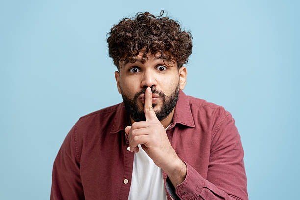 Young adult man making shush gesture keeping a secret or confidential information quiet