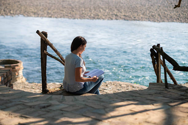Young woman sitting by a river, enjoying a peaceful moment reading a book