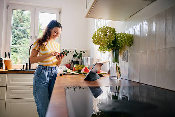 istock Young woman in kitchen checking recipe on her phone while preparing meal 2249691727